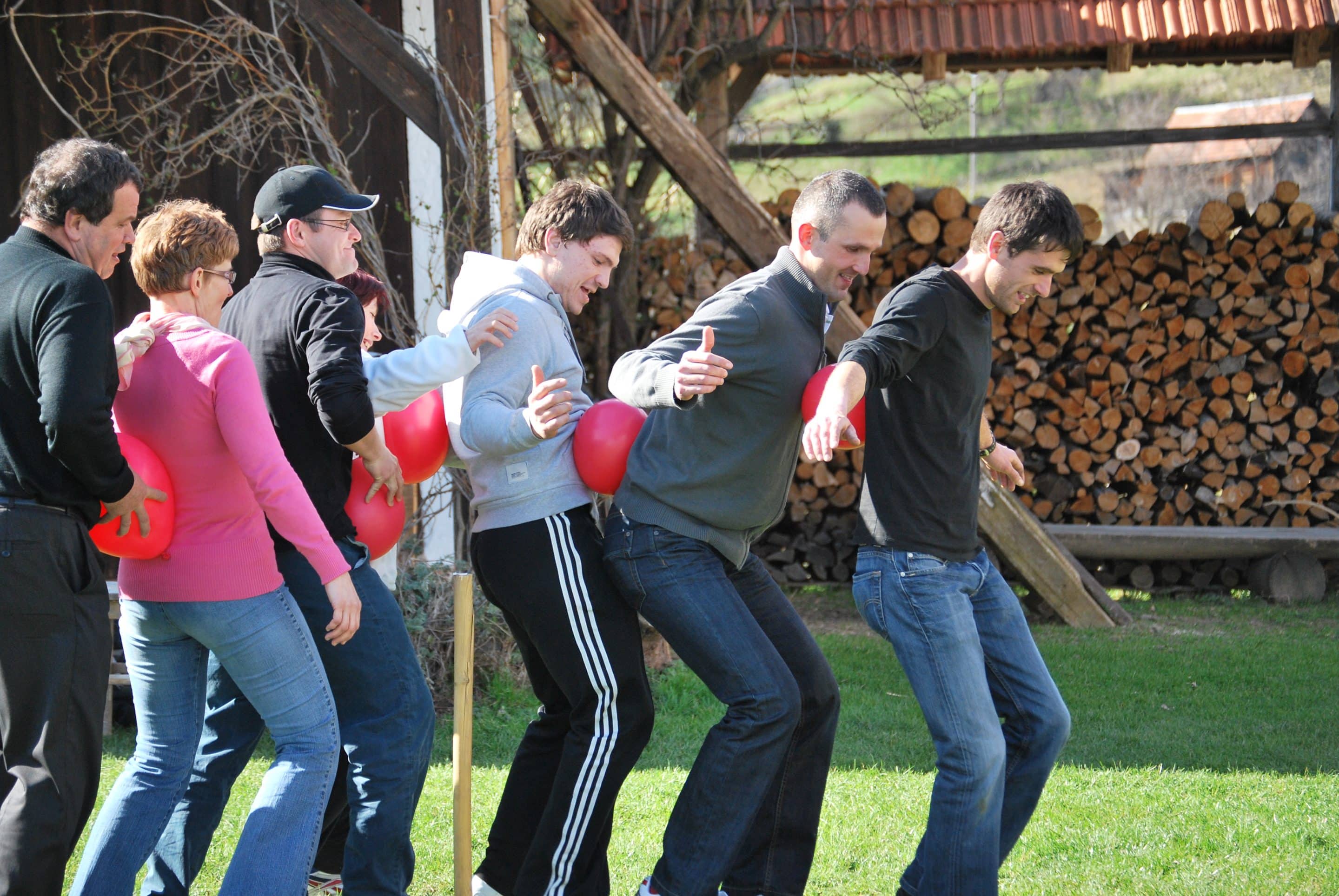 Skupina ljudi med teambuilding igro z rdečimi baloni na travniku.