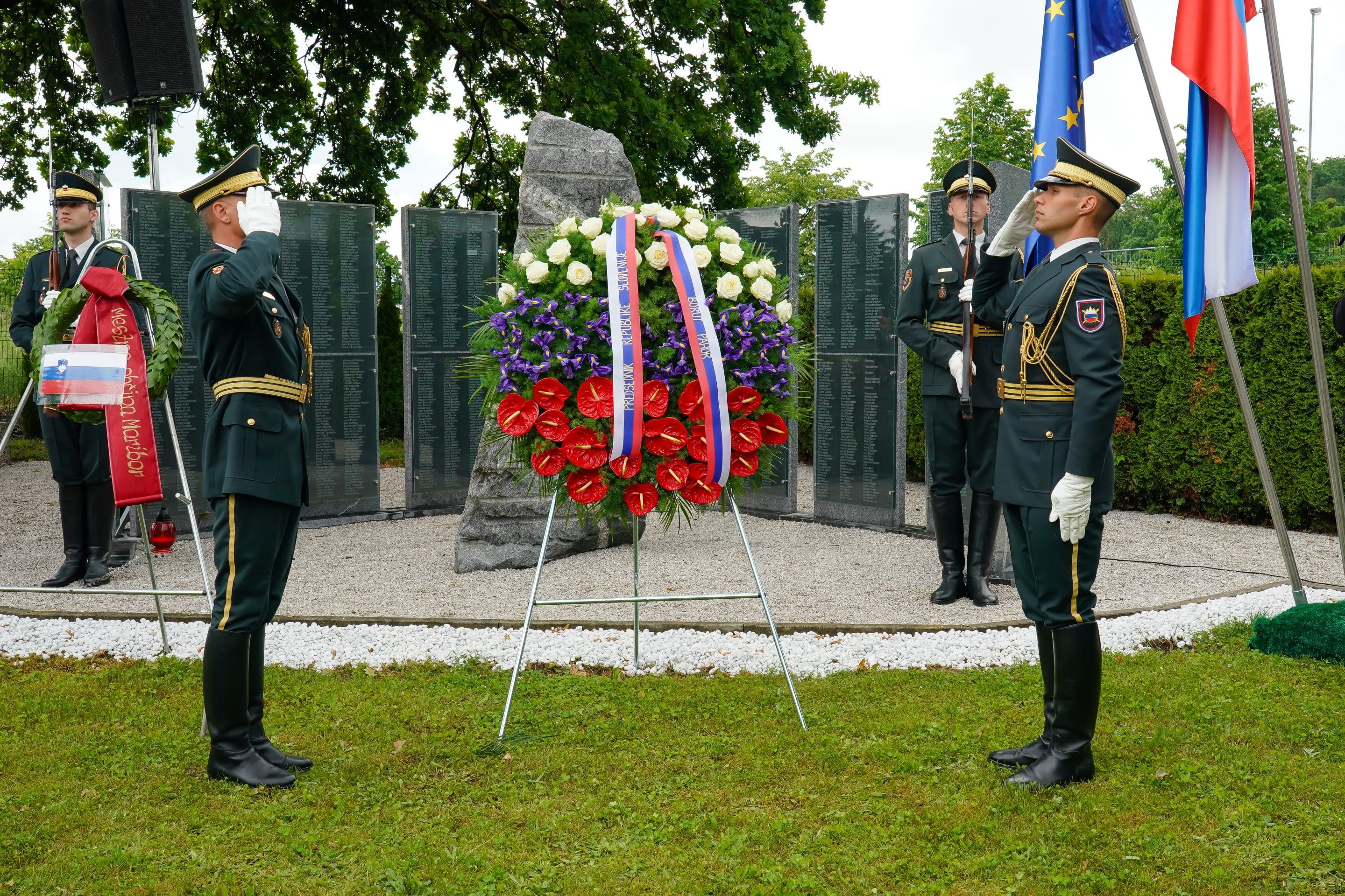 Slovenski vojaki v častni uniformi salutirajo pred vencem ob spomeniku med spominsko slovesnostjo.