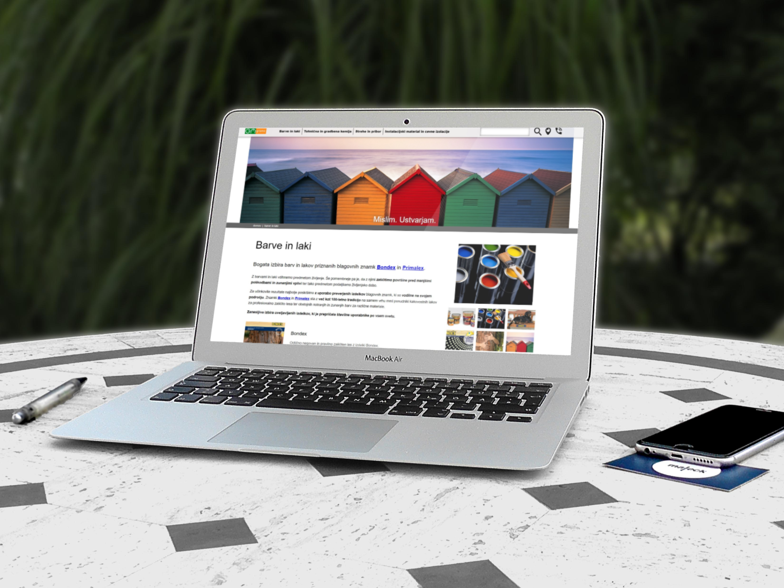 Prenosnik MacBook Air s prikazom prenovljene spletne strani Barve in laki na zunanji mizi.