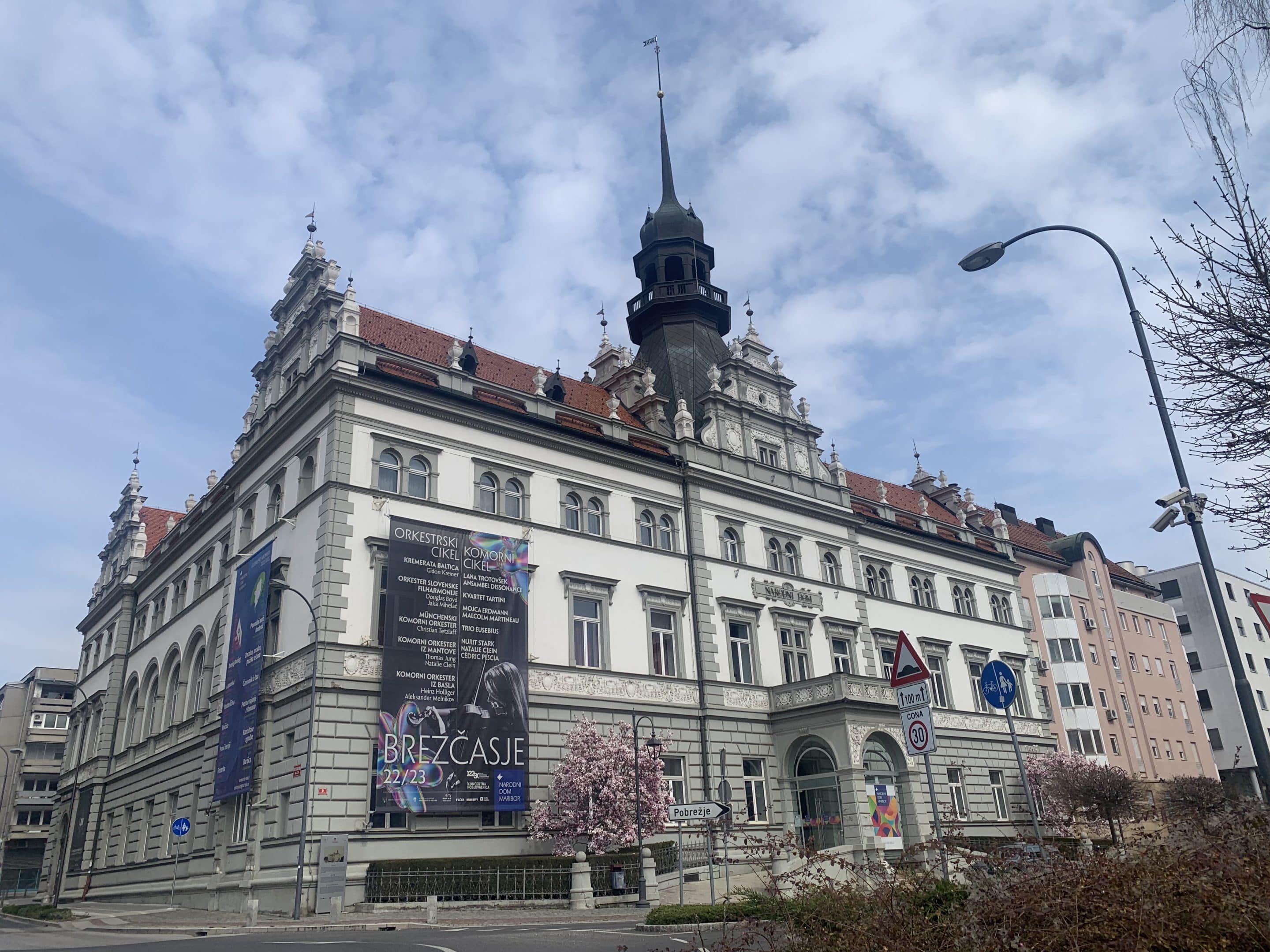 Zgodovinska stavba Narodnega doma v Mariboru z neorenesančno arhitekturo in velikimi plakati za dogodke na fasadi.