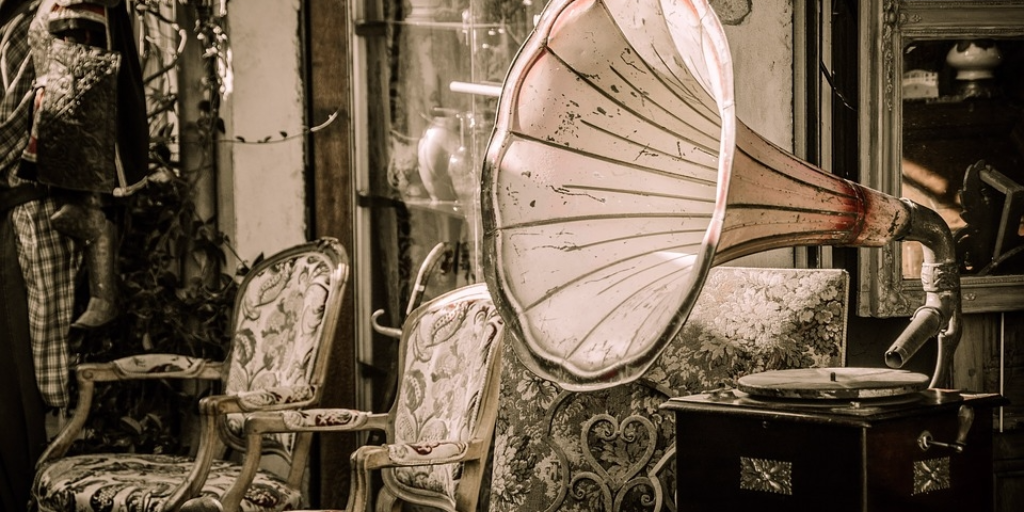 Starinski gramofon z velikim lijakom poleg retro oblazinjenih stolov v sepia tonih.