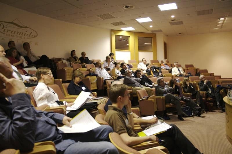 Udeleženci predavanja sedijo v dvorani Hotela Piramida in poslušajo predstavitev na strokovni konferenci.