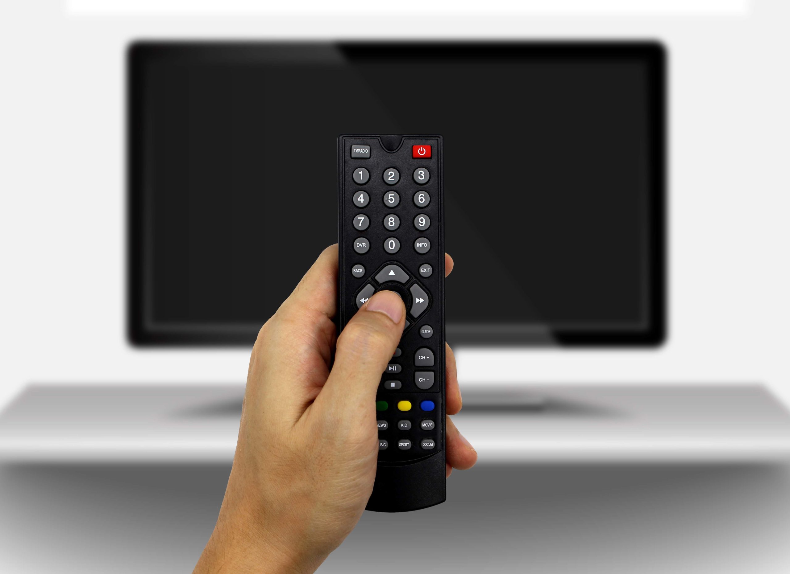 Roka drži črn daljinski upravljalnik, usmerjen proti zamegljenemu zaslonu pametne televizije.