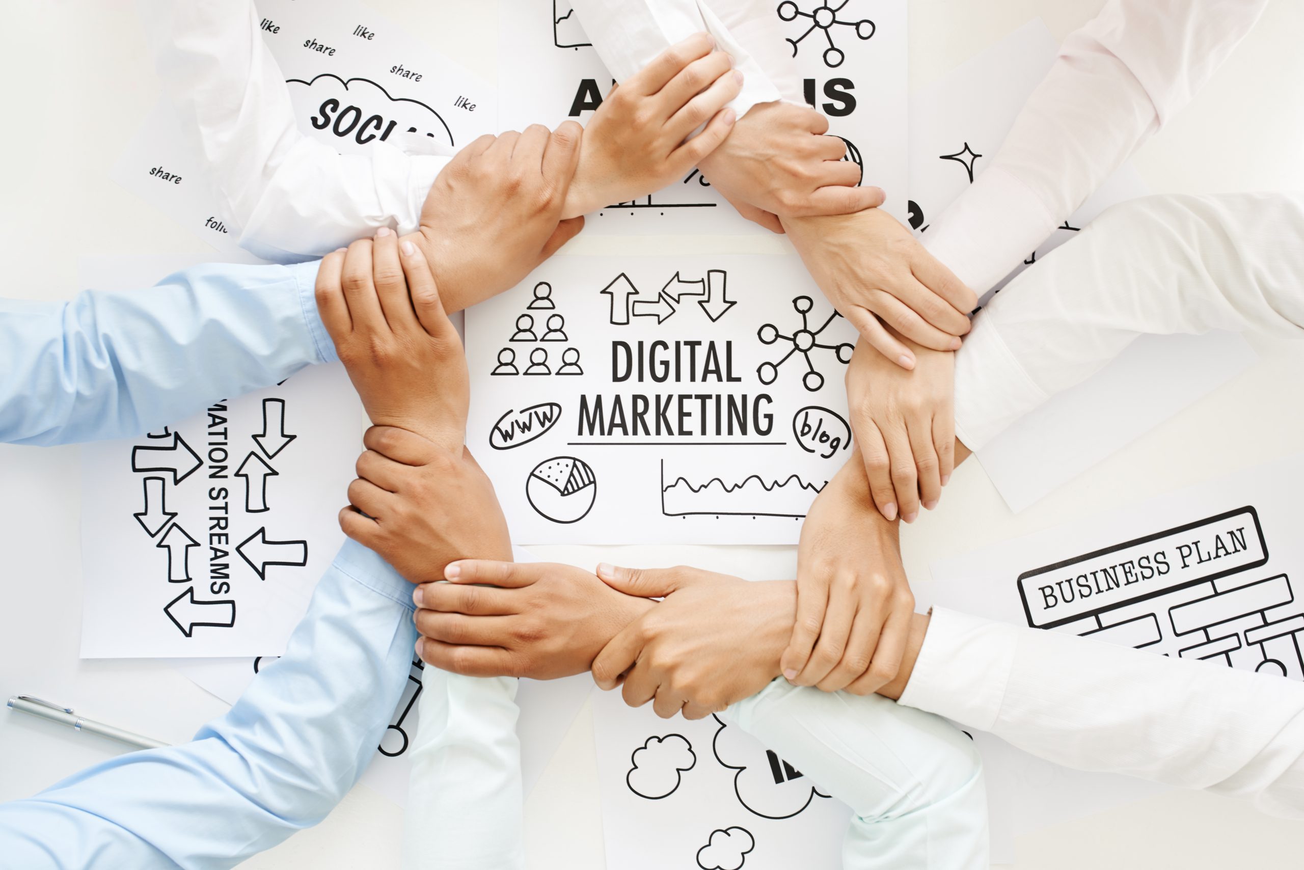 Roke, ki se držijo za zapestja v krogu nad načrtom za digitalni marketing.