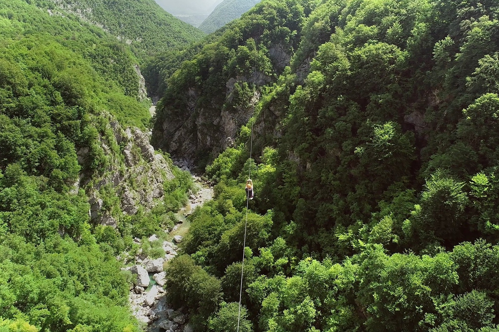 Oseba na spustu po jeklenici visoko nad globoko, zeleno sotesko s kamnitim rečnim dnom.